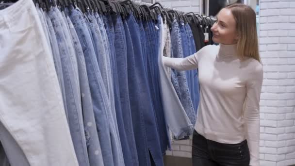 Chica sonriente comprador elegir nuevos pantalones vaqueros en la tienda — Vídeo de stock