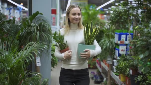 Egy nő sétál át a bolton, kezében két cserép virággal.. — Stock videók