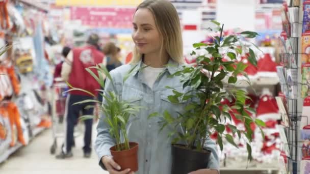 Kobieta wchodzi do sklepu, trzymając dwa doniczki roślin.. — Wideo stockowe