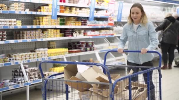 Hermosa joven feliz divirtiéndose montando en el carrito de compras en el supermercado — Vídeo de stock