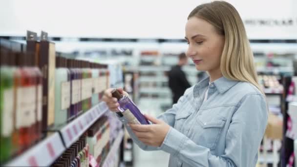 Compras - mujer joven sosteniendo botella de champú en el supermercado — Vídeo de stock