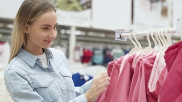 Vrouwelijke koper kiest kleding voor haar kind bij kinderkleding winkel — Stockvideo