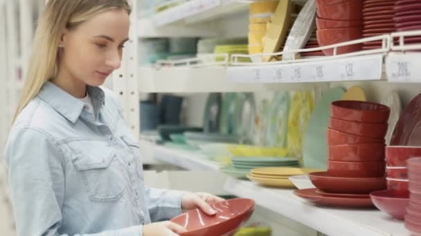 Una mujer compra platos en la tienda, examina varios artículos de platos . — Vídeo de stock