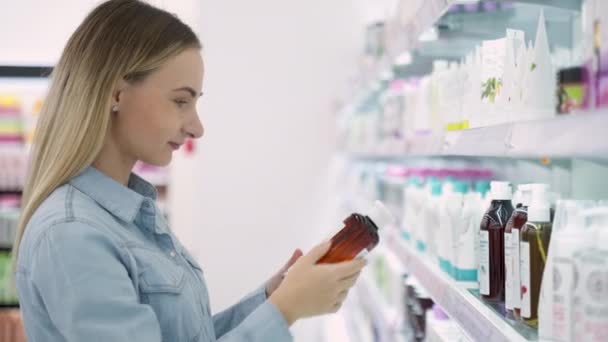 Compras - mujer joven sosteniendo botella de champú en el supermercado — Vídeos de Stock