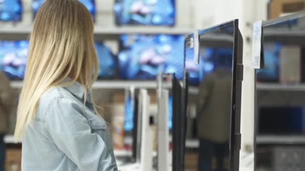 Cliente feminino moderno inteligente escolhendo grandes aparelhos de TV na loja de eletrônicos — Vídeo de Stock