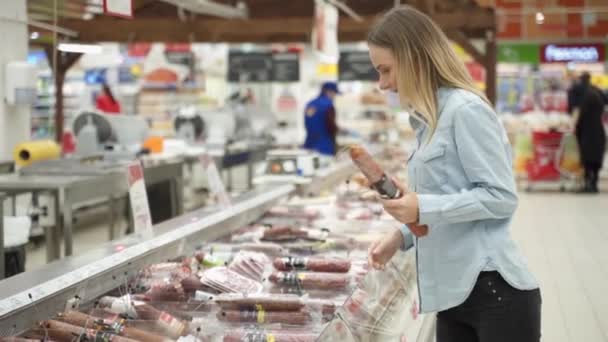 Glückliche Frau betrachtet Fleischprodukte in Vitrine und kauft Pfefferoni-Wurst im Lebensmittelladen — Stockvideo