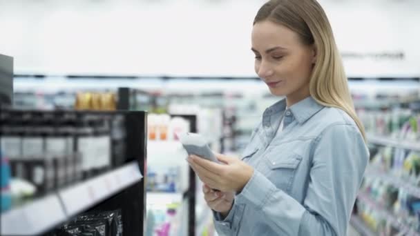 Mujer joven en la tienda de cosméticos está eligiendo crema para el cuidado de la piel . — Vídeos de Stock