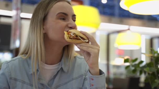 Посмішка Жінка - блондинка годує бургер у кафе швидкого харчування — стокове відео