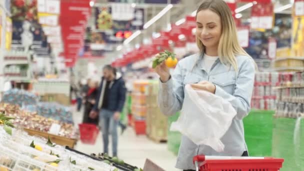 Ung kvinna väljer färsk mandarin i mataffären. — Stockvideo