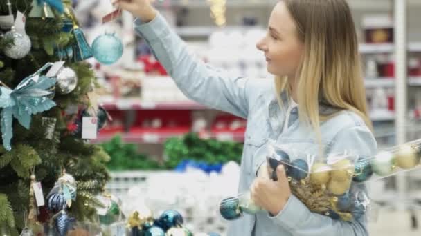 Menina atraente jovem na loja escolhe um brinquedo, decoração de Natal. Preparação para as férias . — Vídeo de Stock