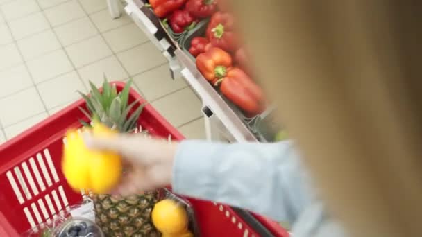 Junge erwachsene Frau, die Paprika in einen Einkaufswagen legt. Ausgeschnittene Ansicht einer jungen erwachsenen Frau beim Einkaufen im Supermarkt. Weibchen legt Paprika in Einkaufswagen — Stockvideo