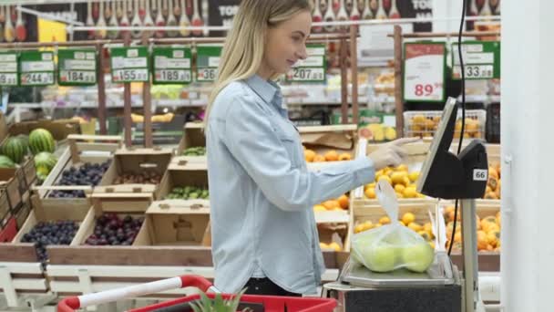 Женщина весит яблоки на весах в продуктовом магазине — стоковое видео