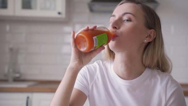 Mujer joven bebiendo jugo de zanahoria en la cocina — Vídeos de Stock