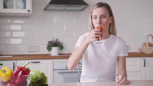 Mujer bebiendo jugo de zanahoria en la cocina — Vídeos de Stock