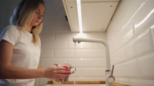 Jovem atraente está lavando pratos enquanto faz a limpeza em casa — Vídeo de Stock