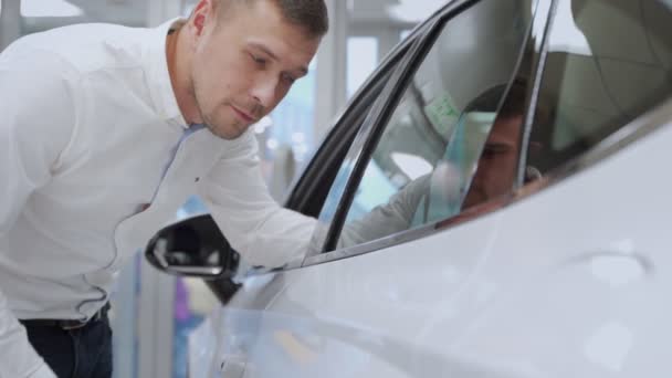 Un homme inspecte sa nouvelle couleur de voiture. Entreprise automobile, vente de voitures, technologie et concept de personnes - homme heureux avec concessionnaire automobile dans le salon ou le salon de l'automobile . — Video