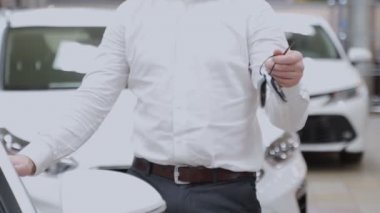 Yeni arabasının anahtarlarını elinde tutan bir müşteri. Araba anahtarlarını elinde tutan adam galeride duruyor.