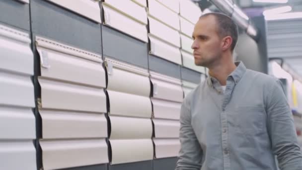 Мужчина выбирает пластиковый сайдинг в магазине — стоковое видео