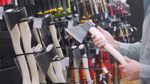 Een jongeman kiest voor bijl in de ijzerwinkel. — Stockvideo