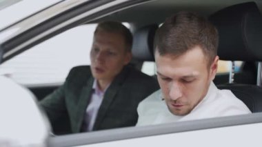 Arabada oturan genç adam. Otomatik iş, araba Satılık, teknoloji ve insan kavramı - auto göstermek ya da salon araba satıcısı ile mutlu erkek. Bir satıcı motor gösterisi ile genç adam.