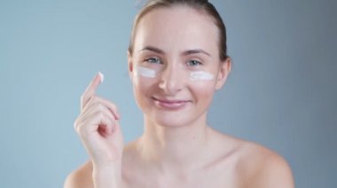 Genç bir kadın yüzüne krem sürüyor. Arka planda izole edilmiş.