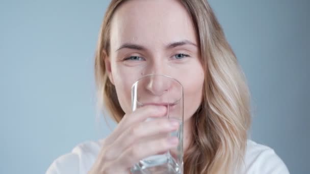 Een vrouw die water drinkt. Glimlachend blank vrouwelijk model met doorzichtig glas in haar hand. Sluitingsdatum. — Stockvideo