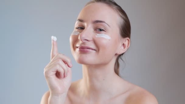 Mujer joven poniendo crema en su cara aislado en el fondo — Vídeo de stock