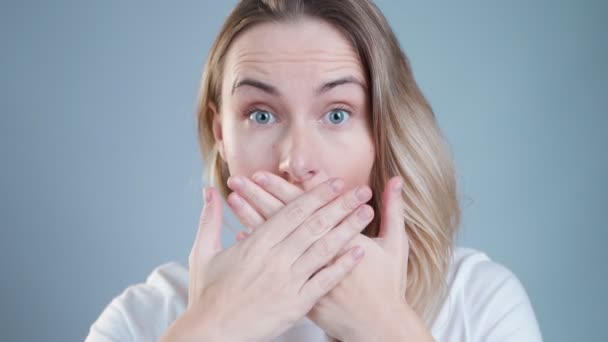 Gros plan portrait de jolie, jolie, mignonne, charmante, femme fermée la bouche avec les mains croisées et les yeux grands ouverts, regardant la caméra, elle ne peut pas croire ses yeux, debout sur fond gris — Video