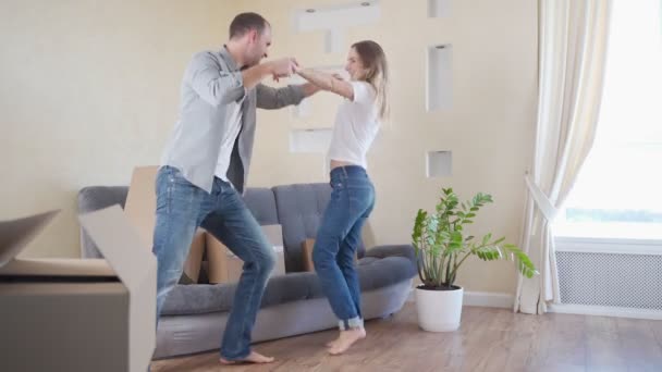 Hermosa pareja joven divirtiéndose bailando en un apartamento nuevo, celebrando mudarse a un nuevo hogar — Vídeos de Stock