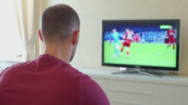 Gergin adam televizyonda maç izliyor, sonuçtan memnun, arkadan bakıyor.