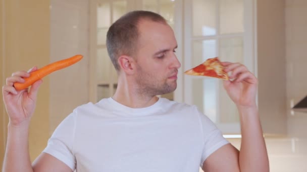 Homem escolhendo pizza ou cenoura na cozinha — Vídeo de Stock