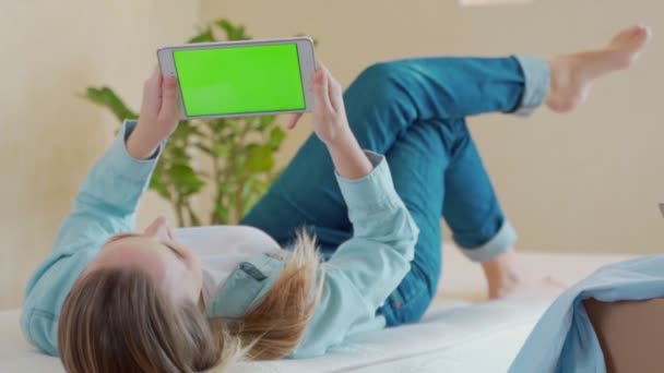 Een vrouw die op een bed ligt met een digitale tablet met een groen scherm — Stockvideo