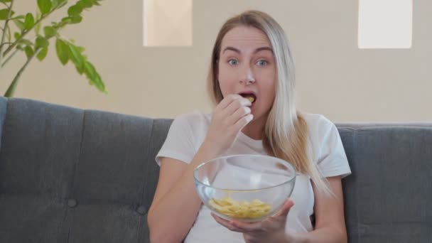 Woman watching TV and eating chips on sofa — Stock Video