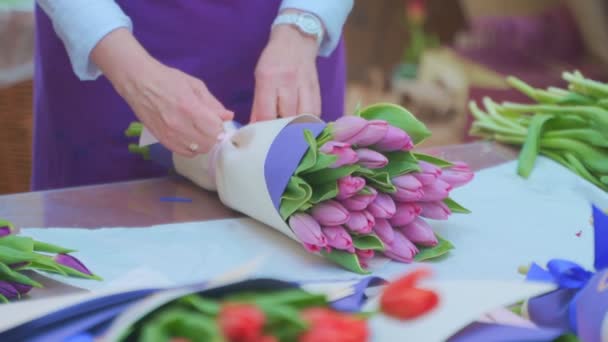 Mujer florista envolviendo hermoso ramo de tulipanes en paquete de papel artesanal — Vídeo de stock