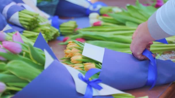 Kobieta kwiaciarnia zawijania piękny bukiet tulipanów w opakowaniu papieru rzemieślniczego — Wideo stockowe
