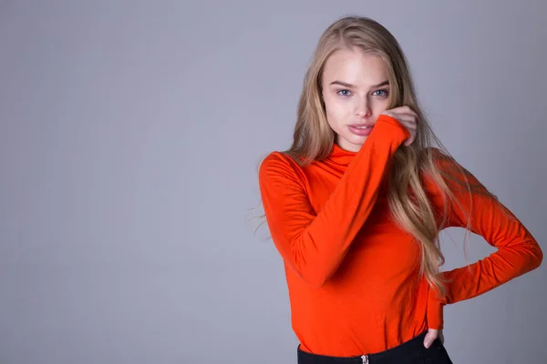 Snyggt porträtt av välklädd moderiktig tjej i orange tröja. Härlig dam poserar inomhus på grå bakgrund. Blond modell med seriös look. Mode och livsstil koncept — Stockfoto