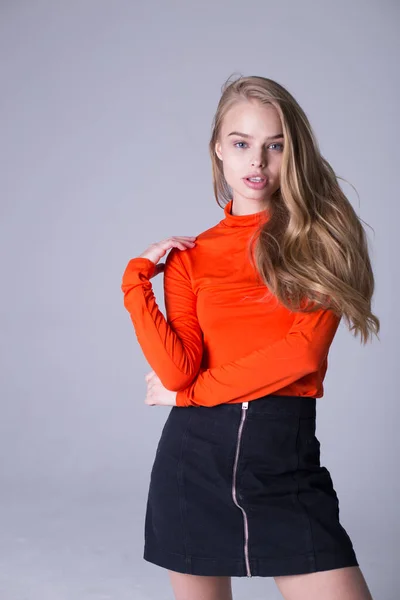 Schönes Porträt eines gut gekleideten modischen Mädchens in orangefarbenem Sweatshirt. Schöne Dame posiert drinnen auf grauem Hintergrund. Blondes Model mit ernstem Blick. Mode- und Lifestyle-Konzept — Stockfoto