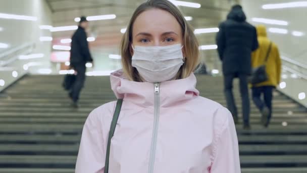 Žena v ochranné sterilní lékařské masce obličeje při pohledu do kamery na stanici metra, virus, pandemický koronavirus koncept — Stock video