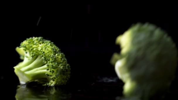 Wiele zielonych świeżych brokułów spada na szklankę z rozpryskami i kroplami wody w zwolnionym tempie na ciemnym tle. Składniki sałatki, zdrowej żywności — Wideo stockowe
