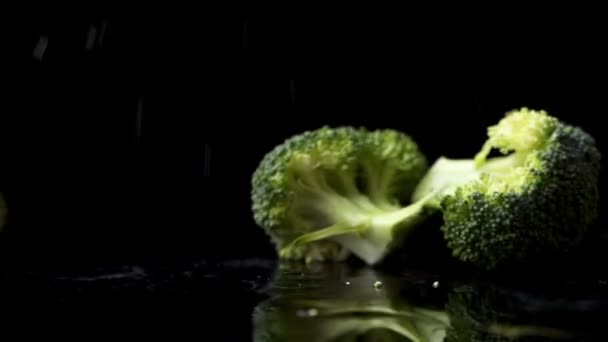 Spousta zelené čerstvé brokolice padá na sklenici s cákanci a kapkami vody ve zpomaleném filmu na tmavém pozadí. Složení pro salát, zdravé potraviny — Stock video