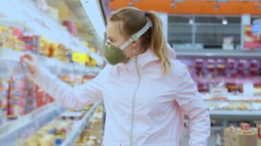 Koruyucu maskeli kız süpermarketteki ürünleri dikkatlice seçiyor, koronovirüs güvenlik önlemlerini karantinaya alıyor