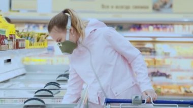 Koruyucu maskeli kız süpermarketteki ürünleri dikkatlice seçiyor, koronovirüs güvenlik önlemlerini karantinaya alıyor
