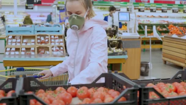 En kvinna i skyddsmask väljer noggrant grönsaker i en stormarknad, karantän coronavirus säkerhetsåtgärder — Stockvideo