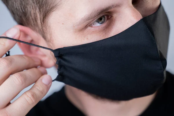 O homem põe uma máscara facial. Máscara facial elegante preto durante uma coroa de vírus pandêmica. Máscara de rosto de algodão artesanal para proteção contra vírus e bactérias . — Fotografia de Stock