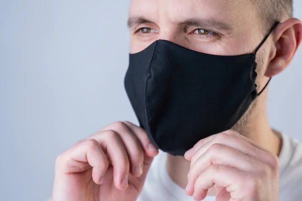 O homem põe uma máscara facial. Máscara facial elegante preto durante uma coroa de vírus pandêmica. Máscara de rosto de algodão artesanal para proteção contra vírus e bactérias . — Fotografia de Stock