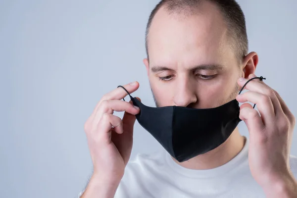 Man puts on a face mask. Black stylish face mask during a pandemic virus crown. Handmade cotton face mask for protection against viruses and bacteria. — Stock Photo, Image