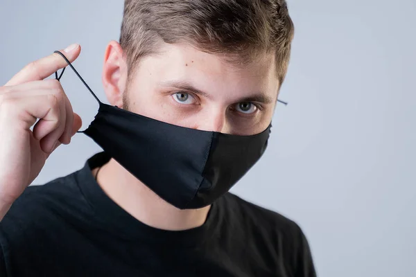 Der Mann setzt sich eine Gesichtsmaske auf. Schwarze, stylische Gesichtsmaske während einer Virenpandemie. Handgemachte Gesichtsmaske aus Baumwolle zum Schutz vor Viren und Bakterien. — Stockfoto