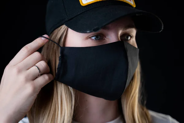 Девушка надевает защитную чёрную маску на лицо, чтобы защитить её от коронавируса. Пандемия коронавируса, ковид-2019 . — стоковое фото