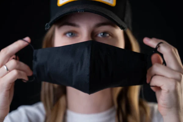 Das Mädchen setzt eine schwarze Schutzmaske über ihr Gesicht, um sie vor dem Coronavirus zu schützen. Coronavirus-Pandemie, Covid-2019. — Stockfoto