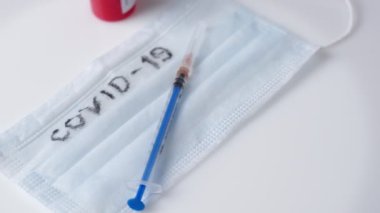 Tıbbi maske, şırınga ve üzerinde kan olan test tüpü beyaz arka planda dönüyor. Covid 19 Yazıtı